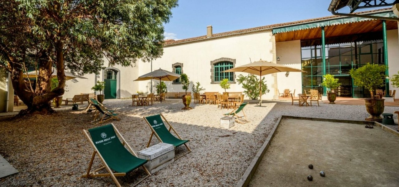 Ambiance en extérieur à Noilly Prat : terrain de pétanque, chaises confortables à l'ombre ou au soleil, avec vue sur le magnifique château en arrière-plan.